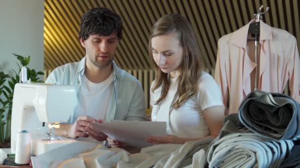 Dos diseñadores de moda - un hombre y una mujer - estaban mirando muestras de bocetos en un taller de costura — Vídeos de Stock