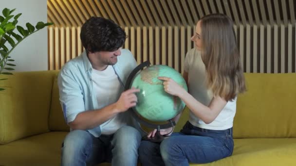 Couple marié regarde le globe dans le salon assis sur le canapé. Jeune couple choisir un endroit pour voyager — Video