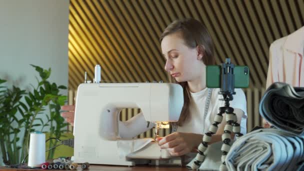Молодая женщина снимает видео-урок, пришивает швейную машинку, ведет блог о шитье — стоковое видео