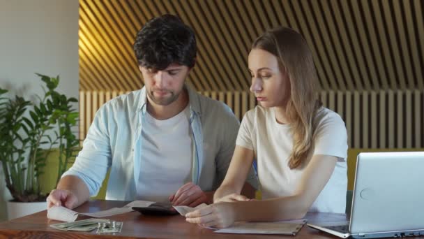 Junge Familie erledigt Papierkram zu Hause. Junges Paar schaut besorgt am Tisch sitzend mit vielen Papierdokumenten, Laptop, Taschenrechner, studiert Rechnung zusammen mit ihrem Mann — Stockvideo