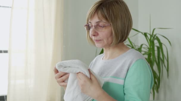 Femme d'âge moyen avec des lunettes renifle une serviette fraîche à la maison — Video