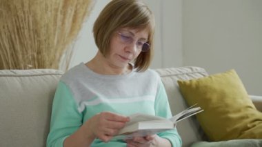 Evde tek başına kitap okuyan kıdemli bir kadın. Orta yaşlı bayan dinleniyor, boş zamanın tadını çıkarıyor, hafta sonunu evde geçiriyor.