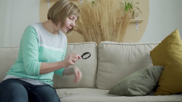 Starší rozrušená žena zkoumá skvrny na pohovce s lupou — Stock video