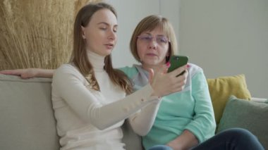 Mutlu yaşlı anne kızıyla kanepede oturmuş akıllı telefonuna bakıyor. Kızı yaşlı bir anneye cep telefonu kullanmayı öğretiyor..