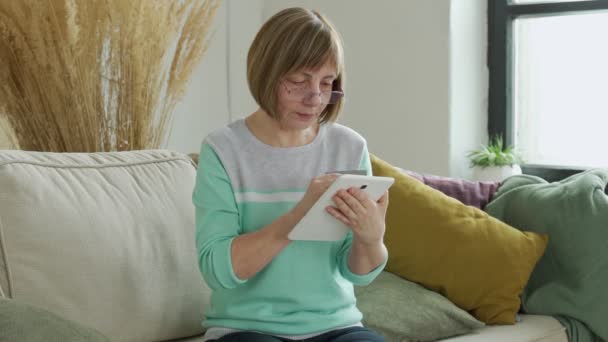 Mujer mayor de compras en línea con tarjeta de crédito utilizando tableta digital. Mujer jubilada moderna sosteniendo tarjeta bancaria mientras compra en línea a través de la tableta — Vídeos de Stock