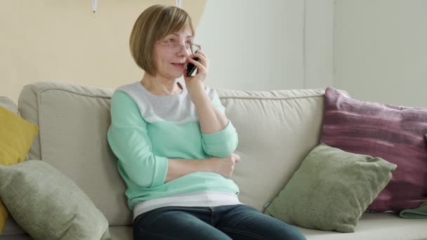 Starsza kobieta rozmawia przez telefon komórkowy siedząc na kanapie, technika komunikacji styl życia — Wideo stockowe