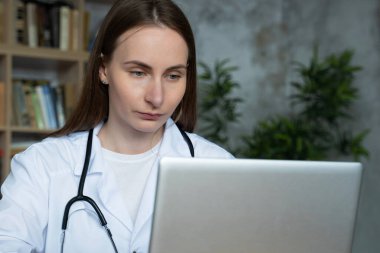 Tıp bürosunda dizüstü bilgisayarını kullanan kadın doktor.