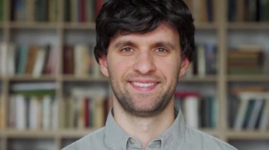 Üniversite kütüphanesinde duran ve kameraya bakan erkek öğrenci.