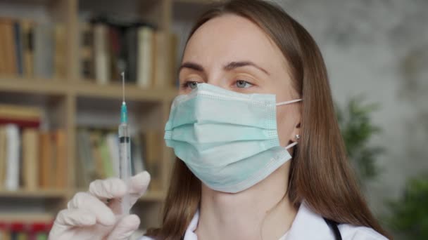 Ärztin mit medizinischer Maske und Schutzhandschuhen, die Spritze mit Medikamenten halten. — Stockvideo