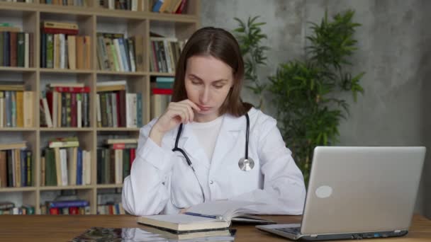 Уставшая женщина-врач, у которой головная боль за столом в клинике — стоковое видео
