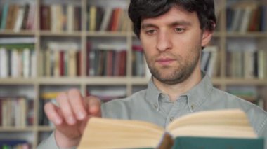 Genç bir erkek öğrenci kütüphanede kitap okuyor. Elinde kitap tutan erkek öğrencinin portresi