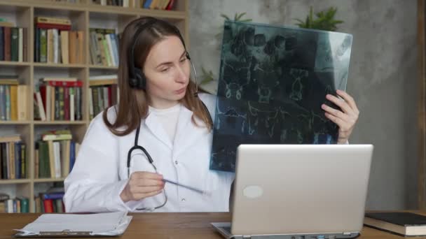 Mujer doctora en auriculares que explica la imagen de rayos X a la paciente durante la videollamada — Vídeos de Stock