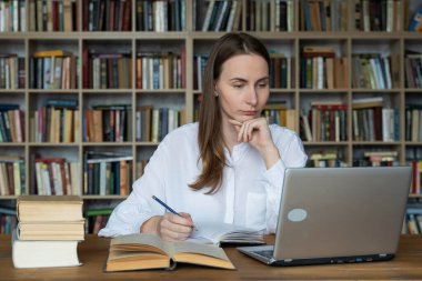 Bilgisayarı kullanan ve internetten öğrenen bir kadın. Genç bayan öğrenci kütüphanede ders çalışıyor.