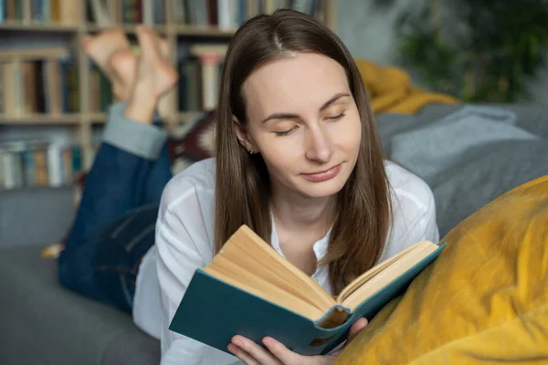 Cerca de la mujer acostada en un cómodo sofá y leyendo un libro emocionante — Foto de Stock