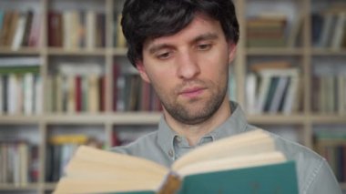 Genç bir erkek öğrenci kütüphanede kitap okuyor. Elinde kitap tutan erkek öğrencinin portresi