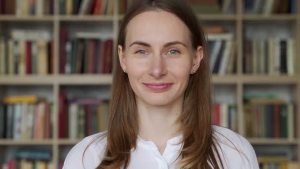 Portrait of young librarian woman smiling at camera in library bookshelf background — Stok Video