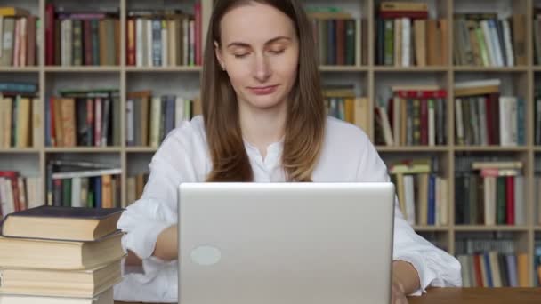 Kobieta korzystająca z laptopa i ucząca się online. Studia dla młodych kobiet w bibliotece — Wideo stockowe