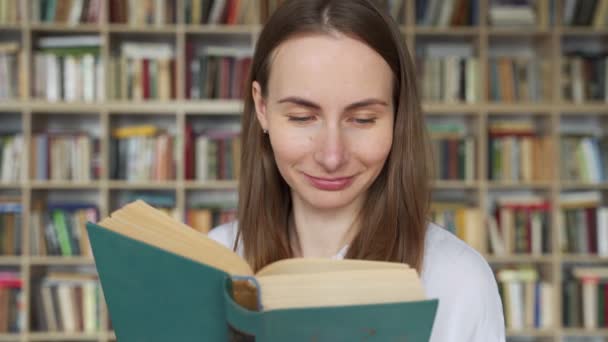 Giovane studentessa che legge un libro in una biblioteca — Video Stock