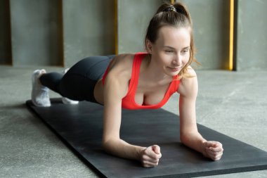 Kadın spor salonunda spor yapıyor. Spor üniformalı genç bir kadın kalas yapıyor.