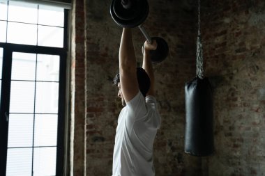 Modern spor salonunda kaslı fitness adamı halteri başının üstüne kaldırıyor. Fonksiyonel eğitim