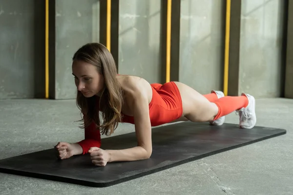 Молодая фитнес-женщина в красном купальнике делает доску на коврике в спортзале — стоковое фото