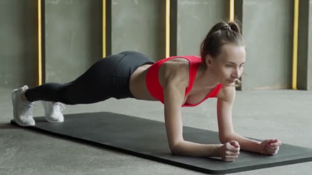 Vrouw sport in de sportschool. Een jonge vrouw in een sportuniform doet een plank — Stockvideo