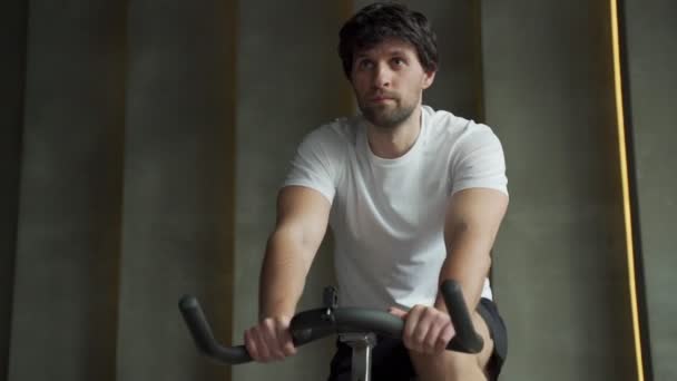 Svalnatý muž, který používá kolo v tělocvičně. Atletický muž ve sportovním oblečení dělá cyklistiku na cvičebních kolech — Stock video