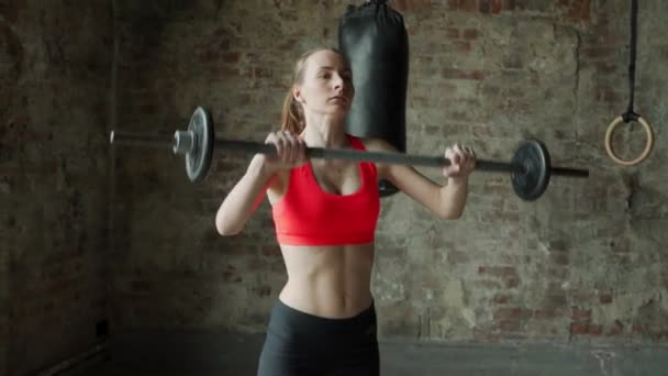 Fitness femme effectue haltérophilie dans la salle de gym. une femme lève un haltère au-dessus de sa tête — Video