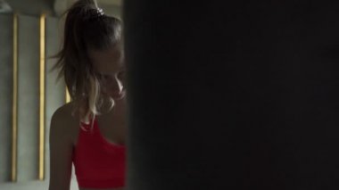 Boks eldivenli kadın kum torbasını yener. Spor giyimli bir kadın, spor salonunda egzersiz yapıyor..