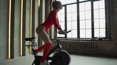 Kırmızı elbiseli atletik kadın spor salonunda aerobik bisiklet egzersizi yapıyor.