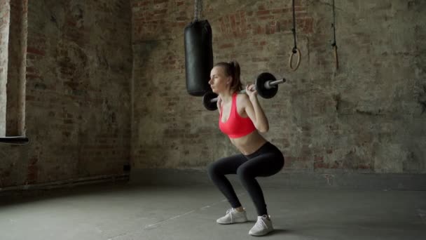 Jonge vrouw doet hurkoefeningen. Atleet vrouw in de sportschool met lange halter — Stockvideo