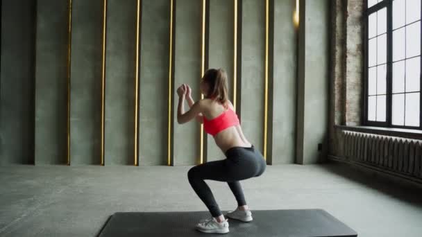 穿着运动服的年轻女运动员蹲在体育馆里.健身锻炼. — 图库视频影像