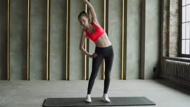 Athlétique jeune femme en tenue de sport échauffer bras tendus stand dans la salle de gym moderne. Jeune belle femme sportive en leggings et un haut fait des exercices d'étirement. — Video