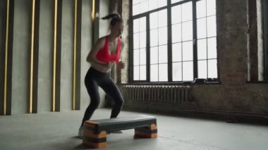 Bir kadın adım platformunda ağır çekimde zıplıyor. Spor salonunda etkin kadın bacakları.