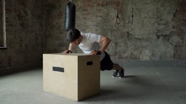 En man som tränar på gymmet gör armhävningar från en trälåda — Stockvideo