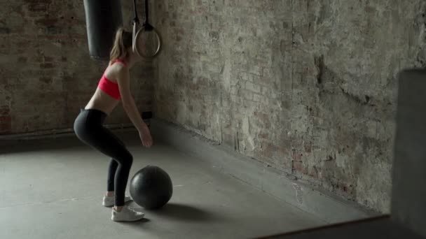 Atleta mulher fazendo agachamentos enquanto joga uma bola de remédio contra uma parede — Vídeo de Stock