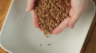 Close-up of a womans hands pouring dry, raw green lentils into a plate.
