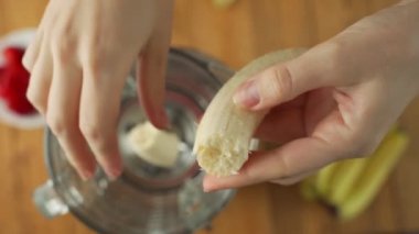 Hand adds fresh banana in a blender to prepare healthy vegan fruit smoothie