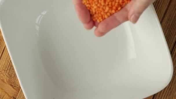 Женские руки наливают сырую красную чечевицу в миску — стоковое видео