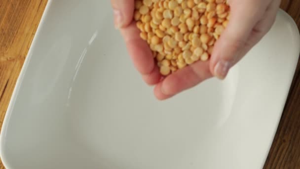 Primer plano de una mujer manos vertiendo granos enteros de guisantes secos en un plato — Vídeo de stock