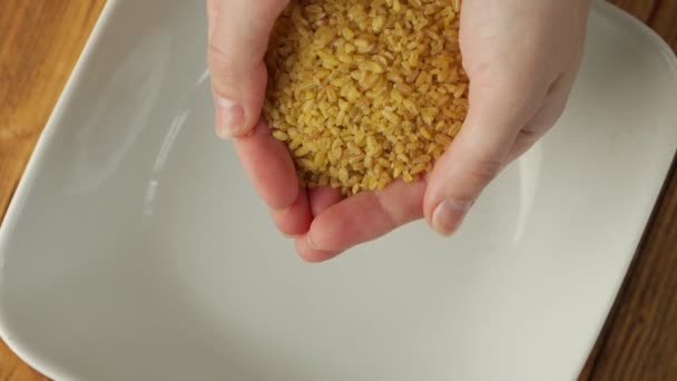 Close-up of a womans hands spilling out dried yellow bulgur wheat grains into a plate, slow motion — Wideo stockowe