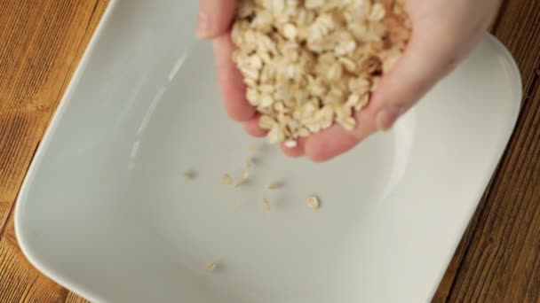 Slow motion video of a womans hands pouring oatmeal into a plate — Stock Video