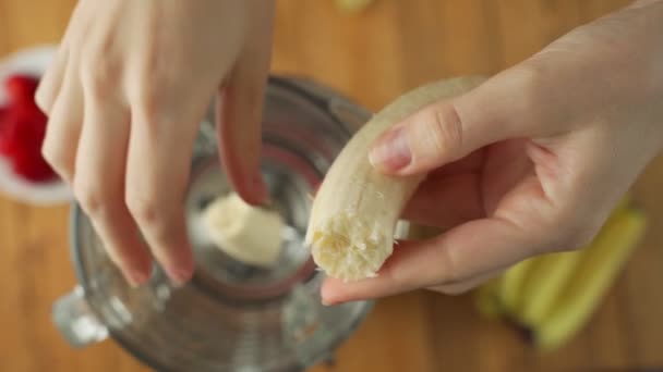 Hand adds fresh banana in a blender to prepare healthy vegan fruit smoothie — Stock video