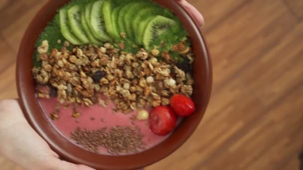 Woman holds a bowl of smoothies with strawberry seeds, kiwi, granola — Stock Video