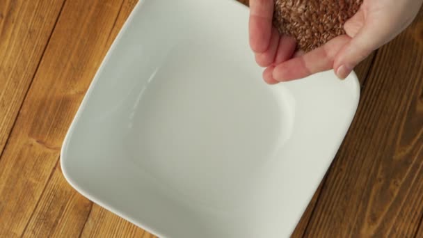 Womens hands pour flax seeds on a plate. Healthy product for the human body. Flax seeds fall to the surface. — Wideo stockowe