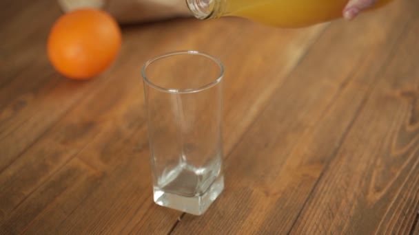 El jugo de naranja se vierte en un vaso de pie sobre una mesa de madera — Vídeos de Stock