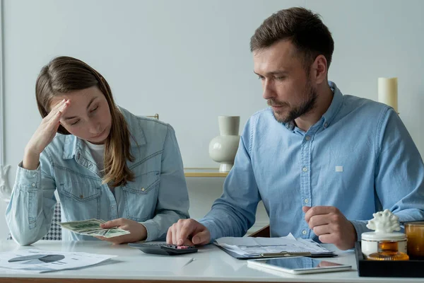 Pareja casada joven sentada en la mesa de la sala de estar, estudiando papeles, hace cálculos en una calculadora, estudia el presupuesto familiar — Foto de Stock