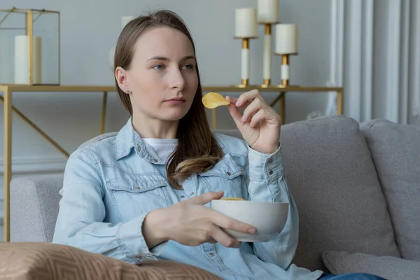 La mujer está sentada en el sofá comiendo papas fritas — Foto de Stock