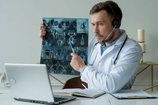 Médico varón escuchando al paciente durante la sesión de telemedicina. Hombre médico que tiene consulta en línea en el ordenador portátil que sostiene la imagen de rayos X y discutir el diagnóstico — Foto de Stock