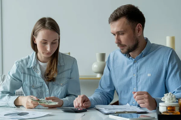 一对年轻夫妇坐在客厅桌旁，研究论文，用计算器进行计算，研究家庭预算 — 图库照片